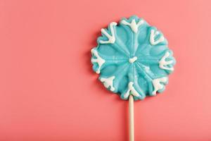 Blue Lollipop in the shape of a snowflake on a pink background. photo