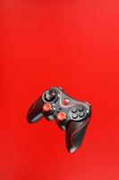 un controlador de juego de joystick negro flota aislado sobre un fondo rojo. entretenimiento interactivo. foto