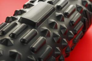 Black lumpy foam massage roller on red background. For the mechanical and reflex effects on tissues and organs. photo