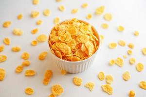 White cup with golden corn flakes, isolated on white background. Hopya crumbled around the cup. View from above photo