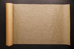 A roll of unfolded brown parchment paper, for baking food in on a dark background, top view. photo