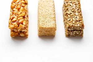 Grain granola bar with peanuts, sesame and seeds in a row on a white background. Top view Three assorted bars, isolate photo