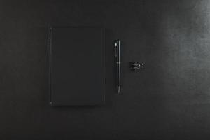 Office desk with black notepad and pen on black background. photo