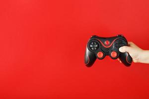 A child's hand holds a gamepad on a red background. Free space, minimalistic creative concept of the Younger generation of gamers. photo