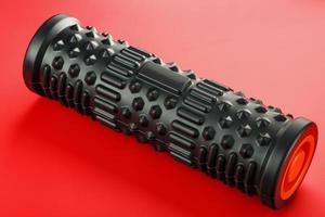 Black lumpy foam massage roller on red background. For the mechanical and reflex effects on tissues and organs. photo