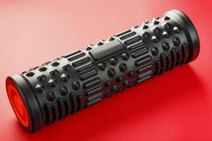 Black lumpy foam massage roller on red background. For the mechanical and reflex effects on tissues and organs. photo