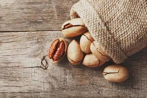 Pecans spill out of a bag on a wooden table, close-up. Peeled, in a shell. photo