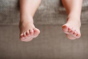 Children's legs close-up hanging from the sofa in the room. Baby toes while baby is sitting on the armchair photo