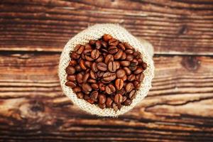 Coffee beans in a burlap bag on a wooden background. photo