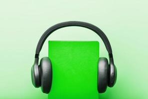 Headphones are worn on a book in a green hardcover on a green background, top view. photo