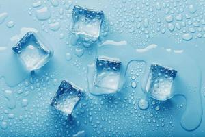 cubos de hielo con gotas de agua derretida sobre un fondo azul, vista superior. foto