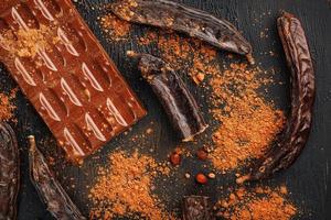 The pods of the carob chocolate bar on a black background. Sweets, chocolate and confectionery made of carob fruit. photo