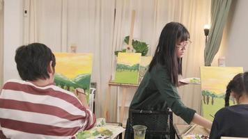 una maestra asiática enseña y demuestra a una estudiante sobre pintura acrílica en color sobre lienzo en el aula de arte, aprendiendo creativamente con habilidad en la educación de estudio de la escuela primaria. video