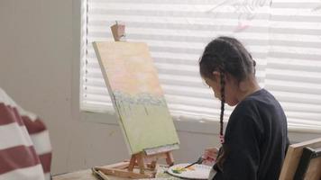 One little girl concentrates on acrylic color picture painting on canvas with multiracial kids in an art classroom, creative learning with talents and skills in the elementary school studio education. video