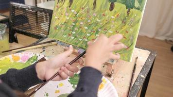 detailopname schot, acryl kleur schilderij techniek, sproeien penseel door hand- Aan canvas, leerling meisje in een kunst klas, elementair school- studio onderwijs met creatief, selectief focus Aan afbeelding. video