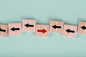 Close up wooden block on blue background with red arrow facing the opposite direction black arrows , Concept of think differently and individual photo