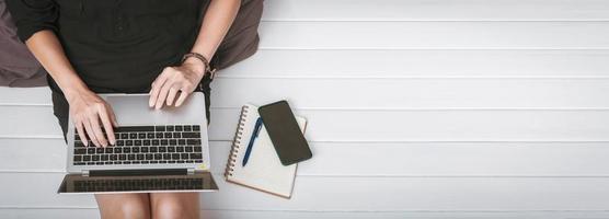 Top view of a young asian woman using laptop computer sitting on wooden floor at home , work from home concept photo