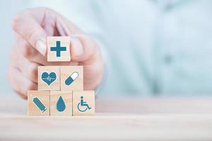 Businessman chooses a emoticon icons healthcare medical symbol on wooden block , Healthcare and medical Insurance concept photo