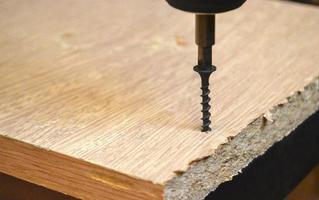 Drills a hole in a chipboard. Drill screwing a screw. photo