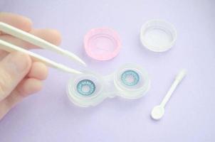 Blue contact lenses in the case. Female hand holds tweezers for contact lens. Bright cosplay lenses. photo