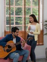 Mixed Race Couple Playing Guitar and Singing Song Together in Living Room at Home photo