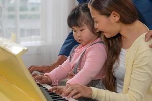 Biracial Family Including Caucasian Father Asian Mother and Child Playing Piano Together at Home photo