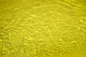 Defocus blurred transparent gold colored clear calm water surface texture with splashes and bubbles. Trendy abstract nature background. Water waves in sunlight with copy space. Gold watercolor shining photo