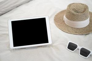 Empty ipad white glasses and brown straw hats on the bed.Holiday concepts photo