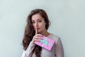 Young positive woman holding small pink gift box isolated on white background. Preparation for holiday. Girl looking happy and excited. Christmas birthday valentine celebration present concept. photo