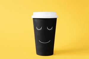 buenos días con café. taza de café desechable con cara sonriente pintada. mañana alegre, bebida vigorizante, amor por el concepto de café foto