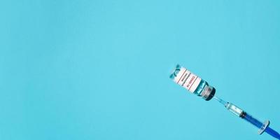 jeringa y vacuna covid-19 sobre fondo azul, puesta plana. banner médico, espacio de copia. concepto de vacunación, inyección