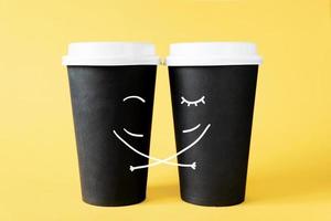 pareja amorosa de tazas de café. abrazando tazas de café desechables sobre un fondo amarillo. concepto creativo de relaciones románticas foto