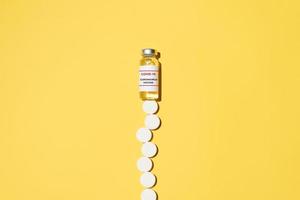 Vaccine vial and many pills on a yellow background. Vaccination and treatment concept. photo