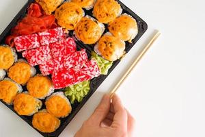 Set of baked and california rolls, top view. Male hand holding chopsticks. Japanese traditional food. photo