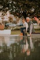 Grandfather spending time with his granddaughter by small water pool in park on autumn day photo