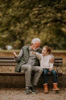 Grandfather spending time with his granddaughter on bench in park on autumn day photo