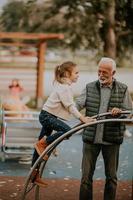 Grandfather spending time with his granddaughter in park playground on autumn day photo