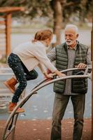 Grandfather spending time with his granddaughter in park playground on autumn day photo