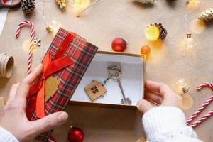 Key to house with keychain on cozy home in gift box with Christmas decor packaging. Pack present for New Year, Christmas. Building, project, moving to new house, mortgage, rent, purchase real estate photo