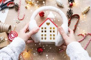 Cozy house in Christmas decor layout, warm knitted scarf, hat, winterization. Winter, snow - home insulation, protection from cold weather, room heating system. Festive mood, Christmas, New Year
