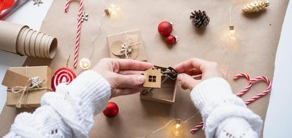 Key to house with keychain on cozy home in gift box with Christmas decor packaging. Pack present for New Year, Christmas. Building, project, moving to new house, mortgage, rent, purchase real estate photo