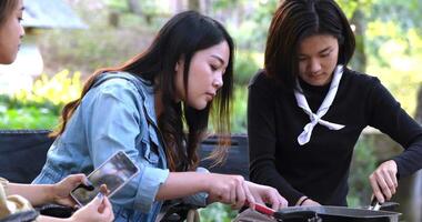 Selective focus hand of young asian woman cut of fried meat and her friend enjoy to eating, They are talk and laugh with fun together while camping in nature park video