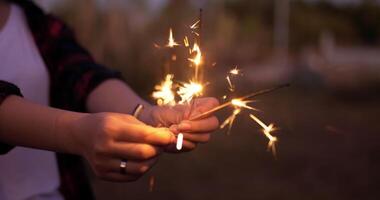 selettivo messa a fuoco, vicino su femmina' mani Tenere e giocare con fuochi d'artificio ardente sparkler mentre godere nel all'aperto nuovo anni festa notte video