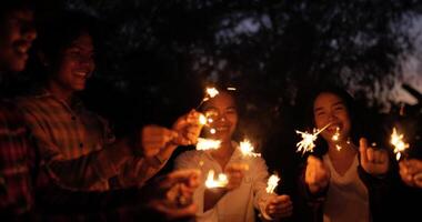 groep van jong vrienden Holding brand brandend sterretjes in nieuw jaar partij, ze zijn blij golvend naar spelen met sparkly in handen, glimlach en lach samen Aan buitenshuis nieuw jaar partij nacht video