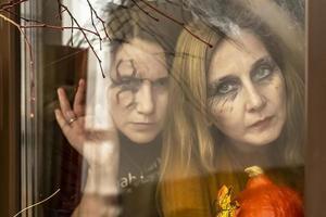 dos brujas miran a través de una telaraña siniestramente por la ventana contra el telón de fondo de las decoraciones de halloween. mascarada, fiesta de halloween foto