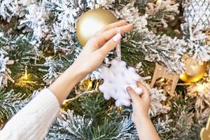 linda niña pequeña y su mamá decoran el árbol de navidad en la casa. familia feliz. foto