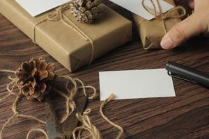 manos masculinas envolviendo regalos de año nuevo y escribiendo tarjetas en una mesa de madera marrón. foto