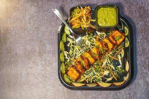 Paneer tikka is an Indian dish made from chunks of paneer with sauce and  vegetables on the table photo