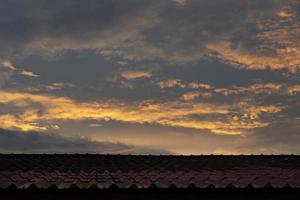 Red roof of an old house under the sky and orange morning clouds. photo