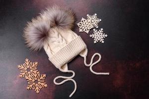 Beautiful white knitted winter cap with pompons on a dark concrete background photo